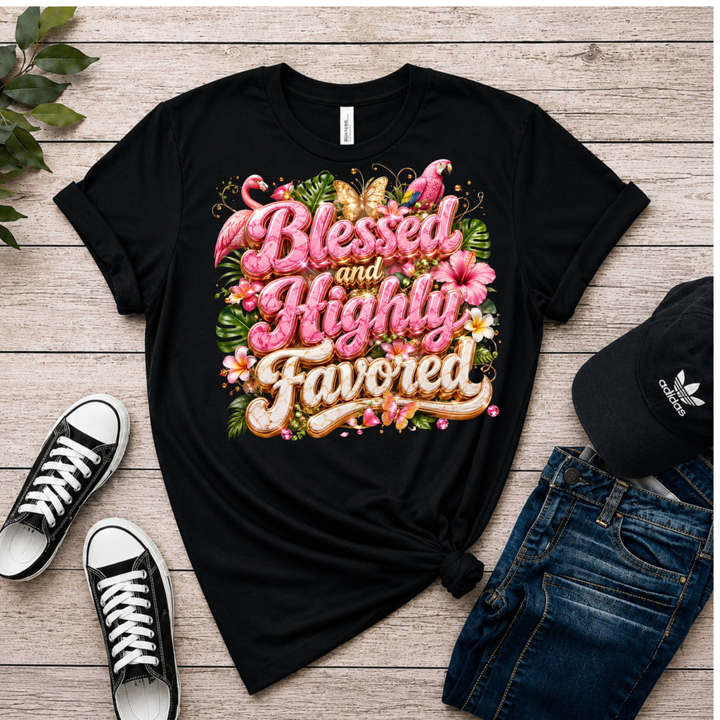 A black graphic T-shirt laid flat on a light wood surface, styled with black sneakers, blue jeans, and a black Adidas cap. The shirt has a large colorful floral and script graphic reading 'Blessed and Highly Favored.