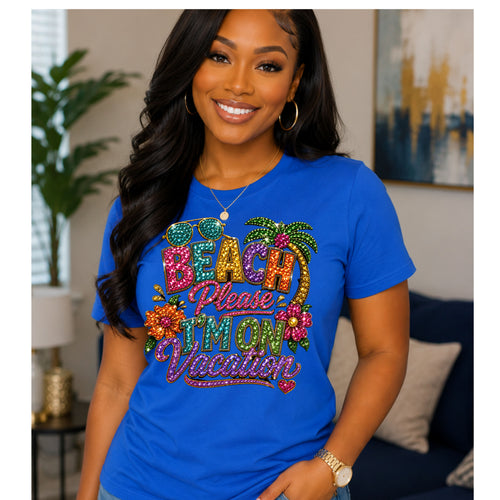A woman wearing blue graphic t-shirt with a colorful, glittery 'Beach Please I'm On Vacation' design, posed in a living room setting.