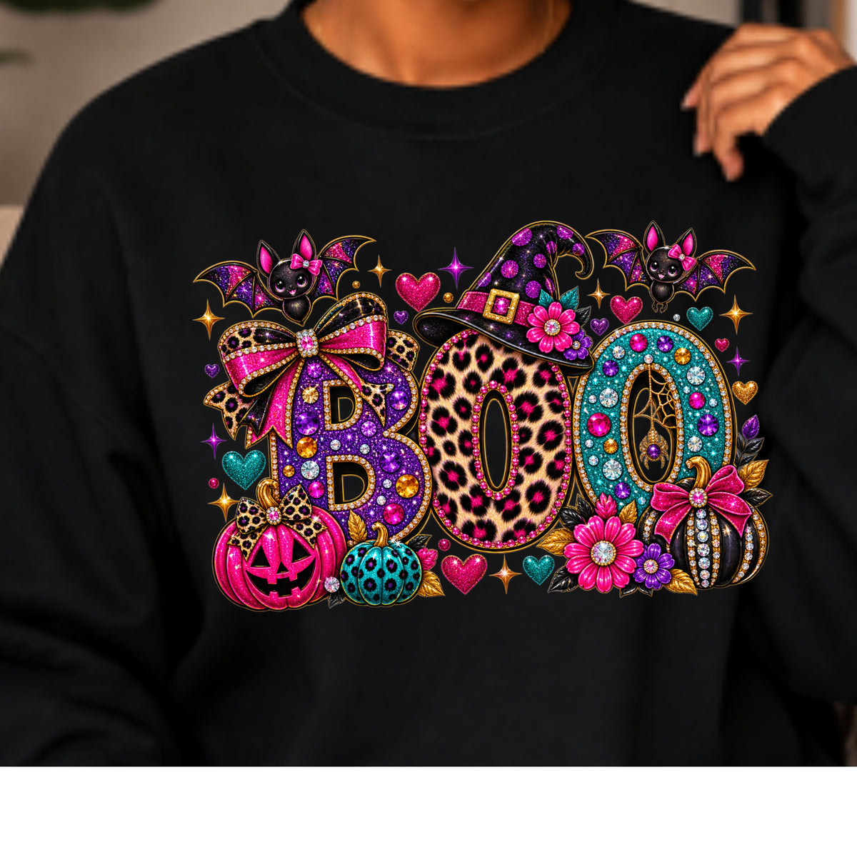 A person wearing a black sweatshirt with a large, vibrant, multicolored graphic spelling 'BOO' decorated with Halloween motifs like pumpkins, bats, and a witch hat.