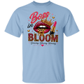 A light blue short-sleeve crewneck t-shirt featuring a colorful graphic print on the front. The graphic displays a pair of leopard-print lips wearing a gold crown, a pink lipstick tube, and the words 'Boss in BLOOM' in pink, gold, and black lettering, with the phrase 'Growing, Glowing, Winning' underneath.