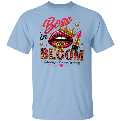 A light blue short-sleeve crewneck t-shirt featuring a colorful graphic print on the front. The graphic displays a pair of leopard-print lips wearing a gold crown, a pink lipstick tube, and the words 'Boss in BLOOM' in pink, gold, and black lettering, with the phrase 'Growing, Glowing, Winning' underneath.