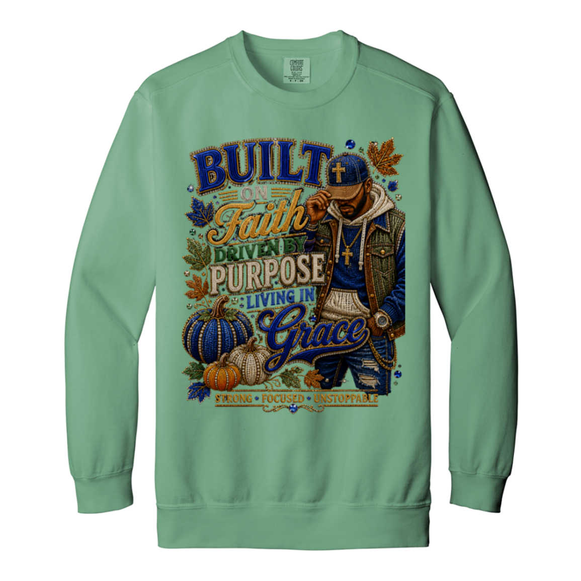 A light green color crewneck sweatshirt featuring a large, detailed graphic print on the front. The graphic displays a man wearing a blue cap and a gold cross, surrounded by autumn elements like pumpkins, leaves, and the text 'BUILT ON Faith DRIVEN PURPOSE LIVING IN Grace'.