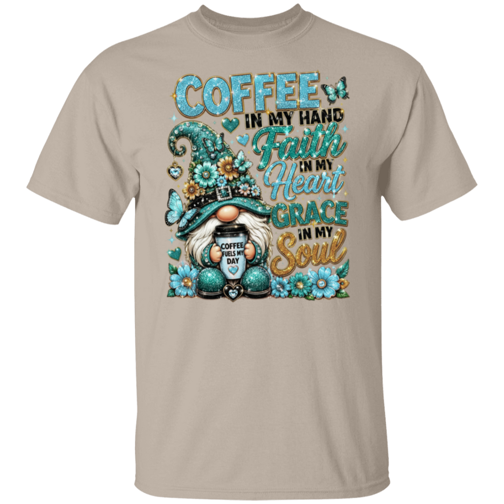 A sand crewneck t-shirt featuring a colorful graphic print of a gnome holding a coffee mug, surrounded by flowers and butterflies, with the text 'COFFEE IN MY HAND Faith IN My Heart GRACE IN My Soul'.