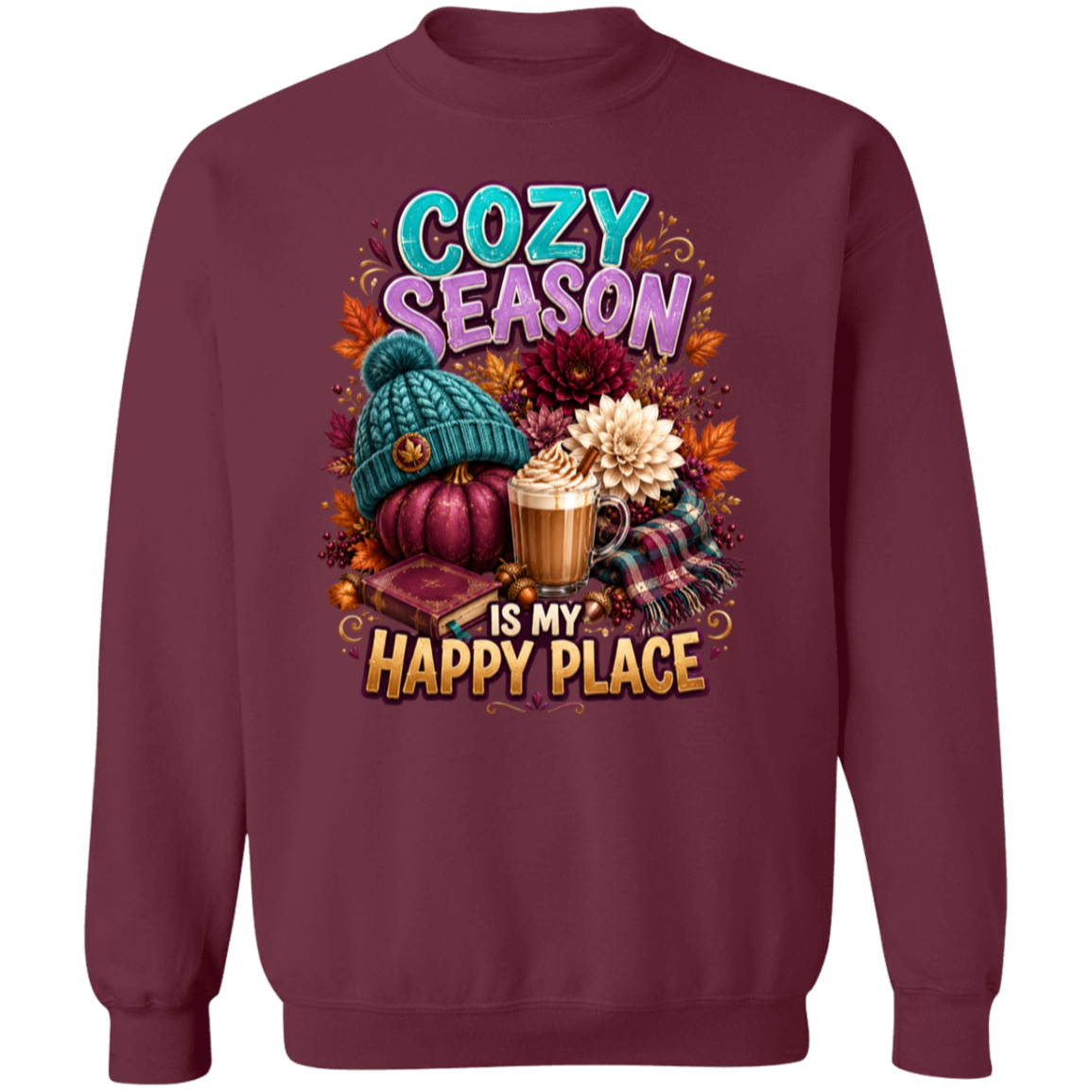 A maroon crewneck sweatshirt featuring a colorful graphic print with autumn and cozy elements, including a teal knit hat, a pumpkin, a hot chocolate cup, and the text 'COZY SEASON IS MY HAPPY PLACE'.