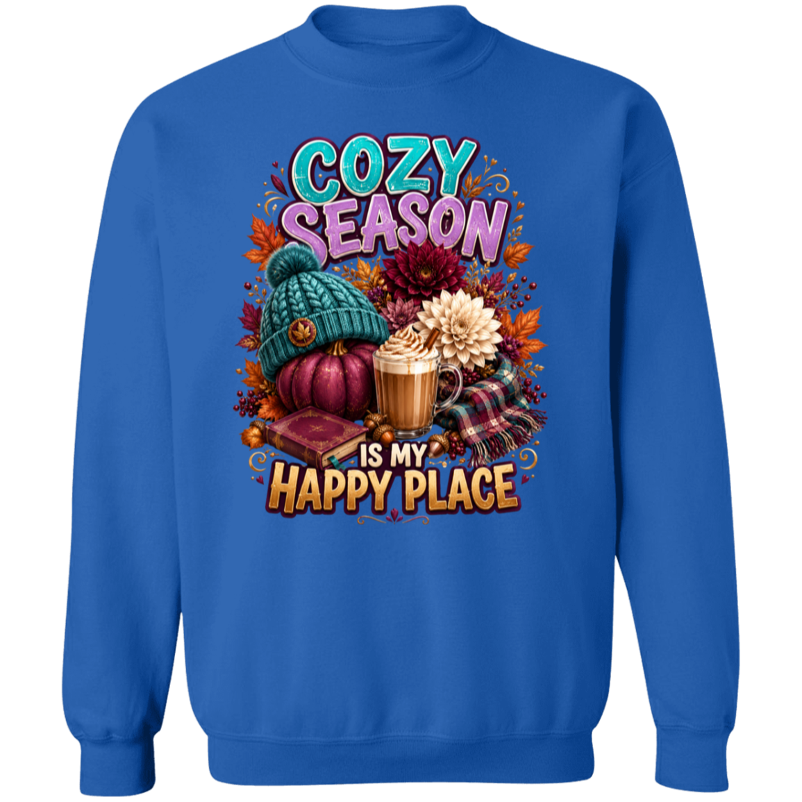 A royal blue crewneck sweatshirt featuring a colorful graphic print on the front with the text 'COZY SEASON IS MY HAPPY PLACE' and autumn-themed illustrations including a teal knit hat, pumpkins, a mug of hot cocoa, plaid fabric, and flowers.