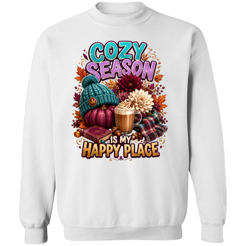A white crewneck sweatshirt featuring a colorful autumn-themed graphic print with the text 'COZY SEASON IS MY HAPPY PLACE' and illustrations of a pumpkin, knit hat, coffee mug, flowers, and plaid fabric.