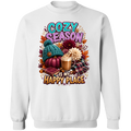 A white crewneck sweatshirt featuring a colorful autumn-themed graphic print with the text 'COZY SEASON IS MY HAPPY PLACE' and illustrations of a pumpkin, knit hat, coffee mug, flowers, and plaid fabric.