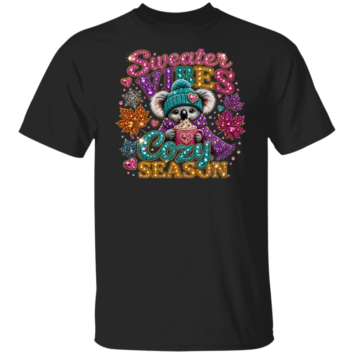 A black short-sleeve crewneck t-shirt featuring a colorful graphic print of a cute koala wearing a teal beanie and holding a mug, surrounded by glittery text that reads 'Sweater VILES Cozy SEASON' and winter-themed embellishments.