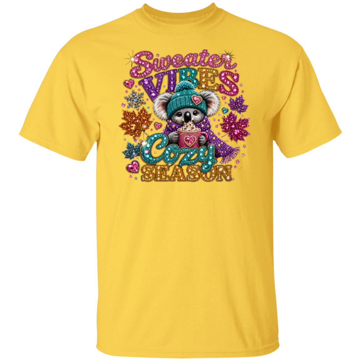 A daisy color short-sleeve crewneck t-shirt featuring a colorful graphic of a cute cartoon koala wearing a teal knit hat and purple scarf, holding a mug with a heart. The graphic reads 'Sweater VIBES Cozy SEASON' in glittery pink, purple, and teal lettering, surrounded by decorative snowflakes and hearts.