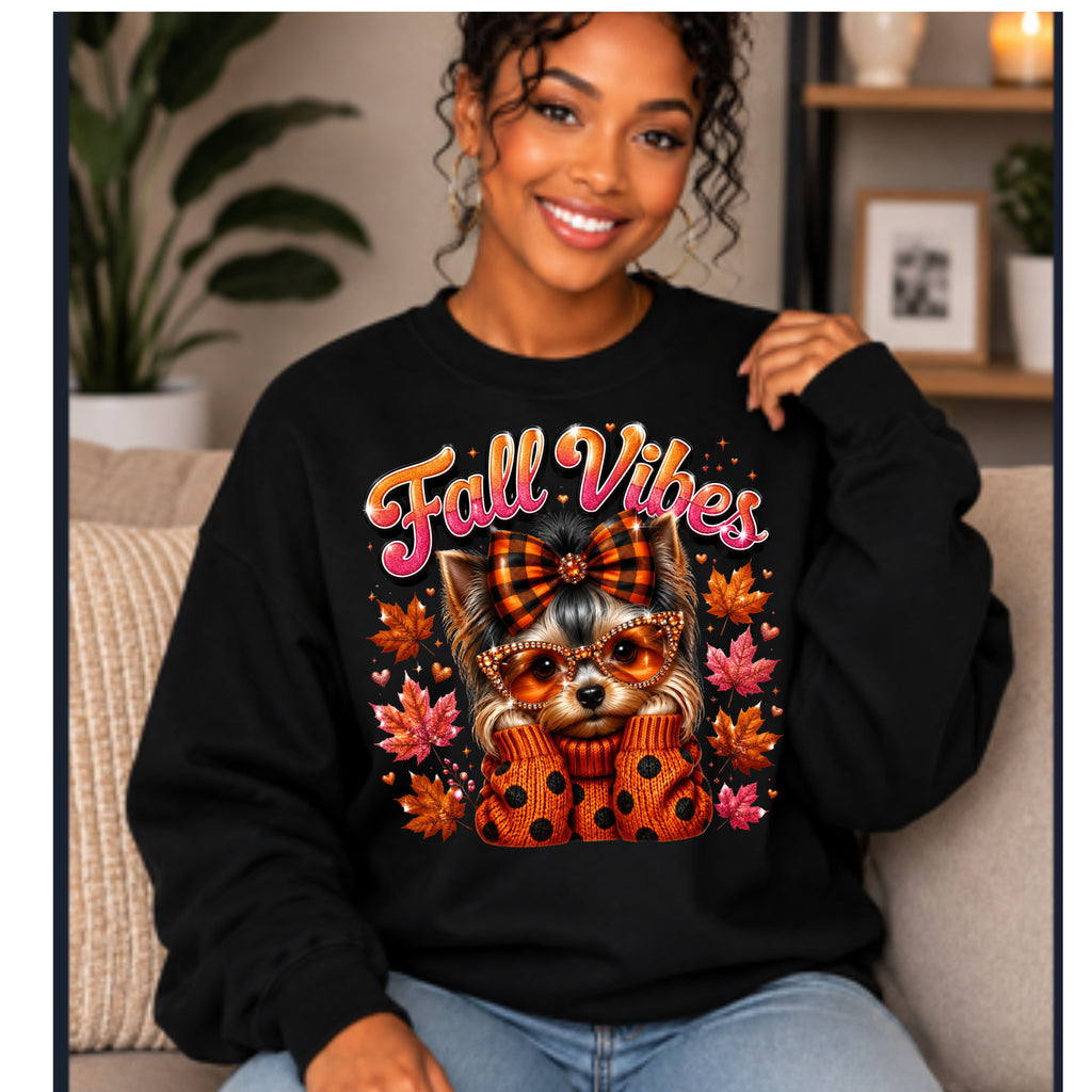 A woman sitting on a couch wearing a black crewneck sweatshirt with a colorful graphic of a cat in an autumn outfit and the words 'Fall Vibes' in orange and pink lettering.