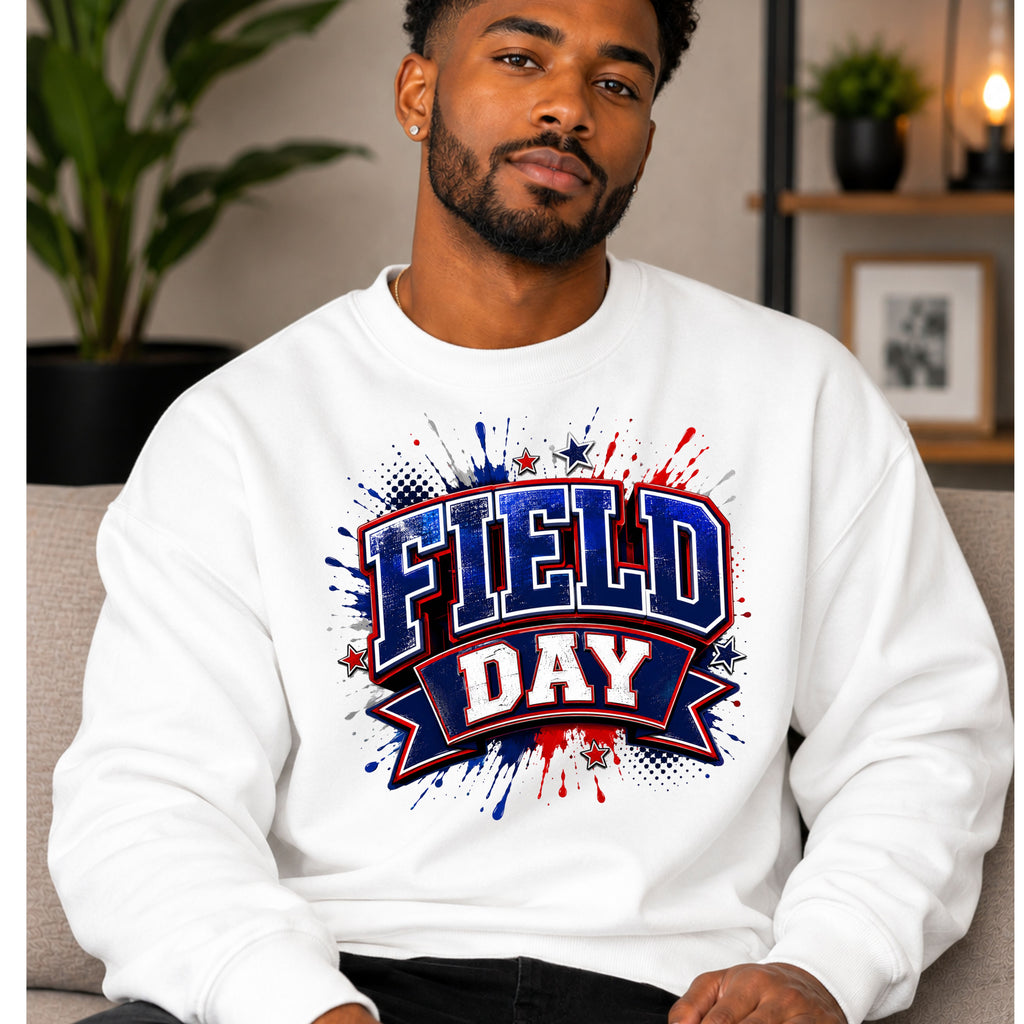 A man wearing a white crewneck sweatshirt with a 'FIELD DAY' graphic in red, white, and blue on the chest, set in a cozy indoor environment.