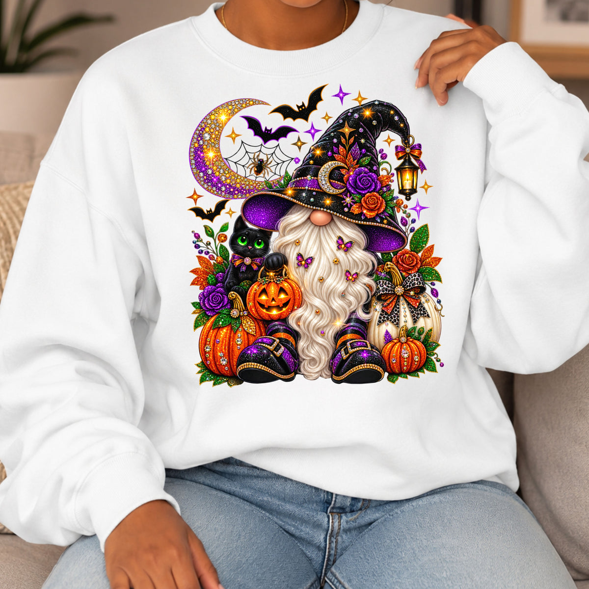 A person wearing a white crewneck sweatshirt with a large, colorful Halloween-themed graphic on the chest. The graphic features a witch with a long white beard, purple hat, black cat, pumpkins, and a crescent moon.