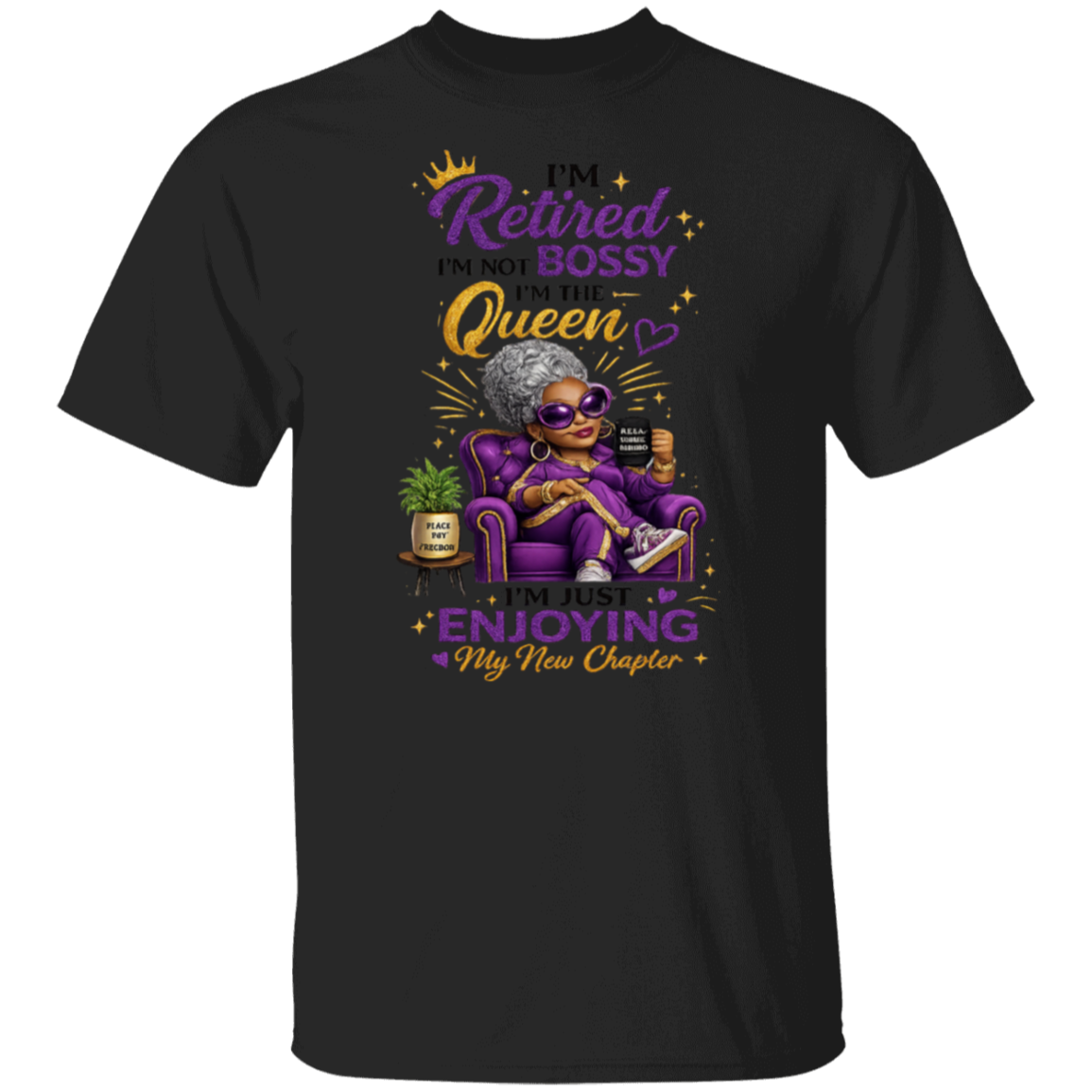 A black short-sleeve t-shirt with a colorful graphic print on the front. The graphic features a cartoon elderly woman in a purple armchair wearing sunglasses and holding a drink, surrounded by text that reads 'I'm Retired I'm NOT BOSSY I'm Queen I'm just ENJOYING My New Chapter' with gold and purple lettering.