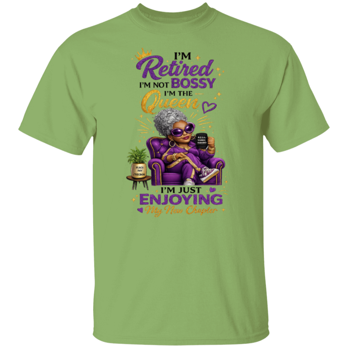 A kiwi short-sleeve t-shirt with a colorful graphic of an elderly woman in sunglasses sitting in a purple armchair, holding a phone. The text reads 'I'M Retired I'M NOT BOSSY I'M THE Queen I'm just ENJOYING My Age!' in purple, yellow, and black lettering.