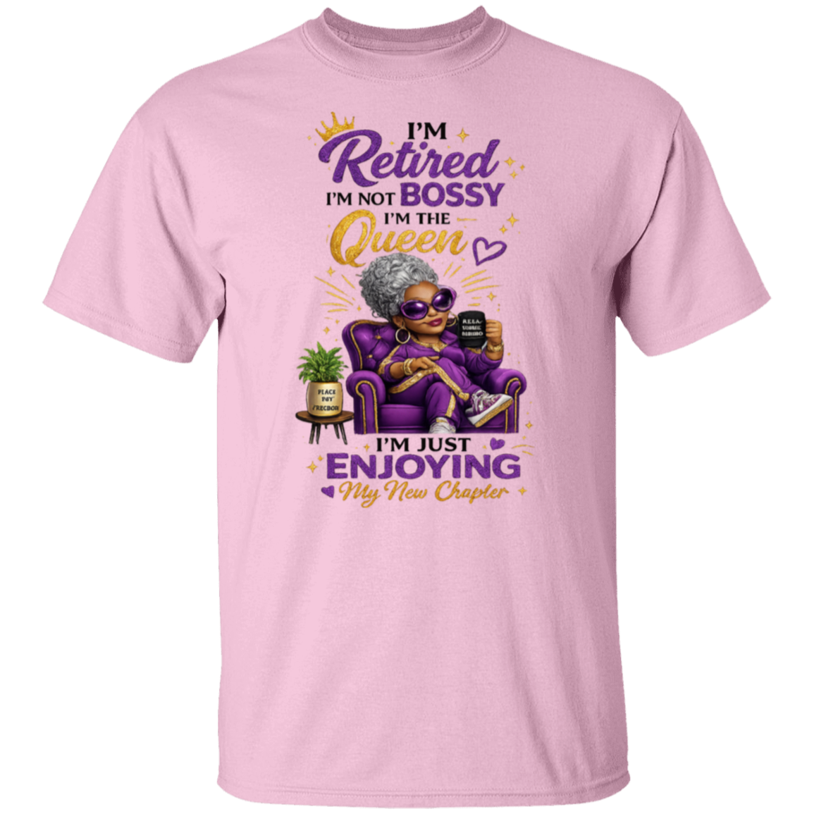 A light pink short-sleeve t-shirt with a colorful graphic of an elderly woman in sunglasses sitting in a purple armchair, holding a phone. The text reads 'I'm Retired I'm NOT BOSSY I'm the Queen I'm just ENJOYING My New Chapter' in purple and gold lettering.