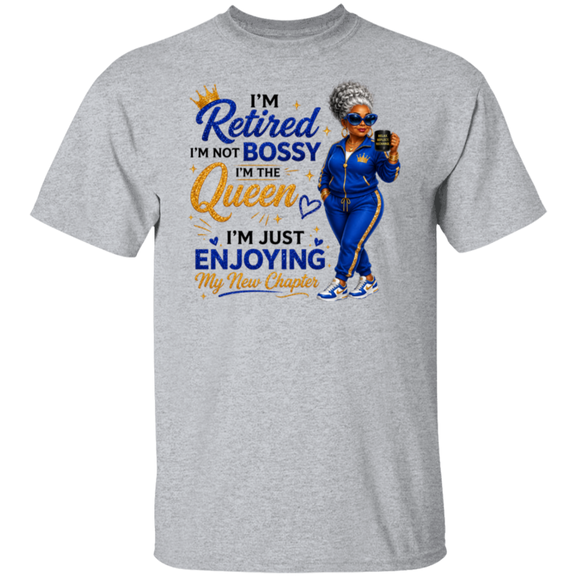 A heather gray short-sleeve t-shirt with a colorful graphic print on the front. The graphic features a cartoon illustration of a woman in a blue tracksuit holding a phone, next to the text 'I'm Retired I'm Not Bossy I'm The Queen I'm Just Enjoying My New Chapter' in blue and gold lettering.