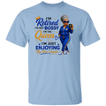 A light blue crewneck t-shirt featuring a colorful graphic print on the front. The graphic displays a cartoon illustration of a woman in a blue tracksuit holding a phone, next to the text 'I'm Retired I'm Not Bossy I'm The Queen I'm Just Enjoying My New Chapter' in blue and gold lettering.