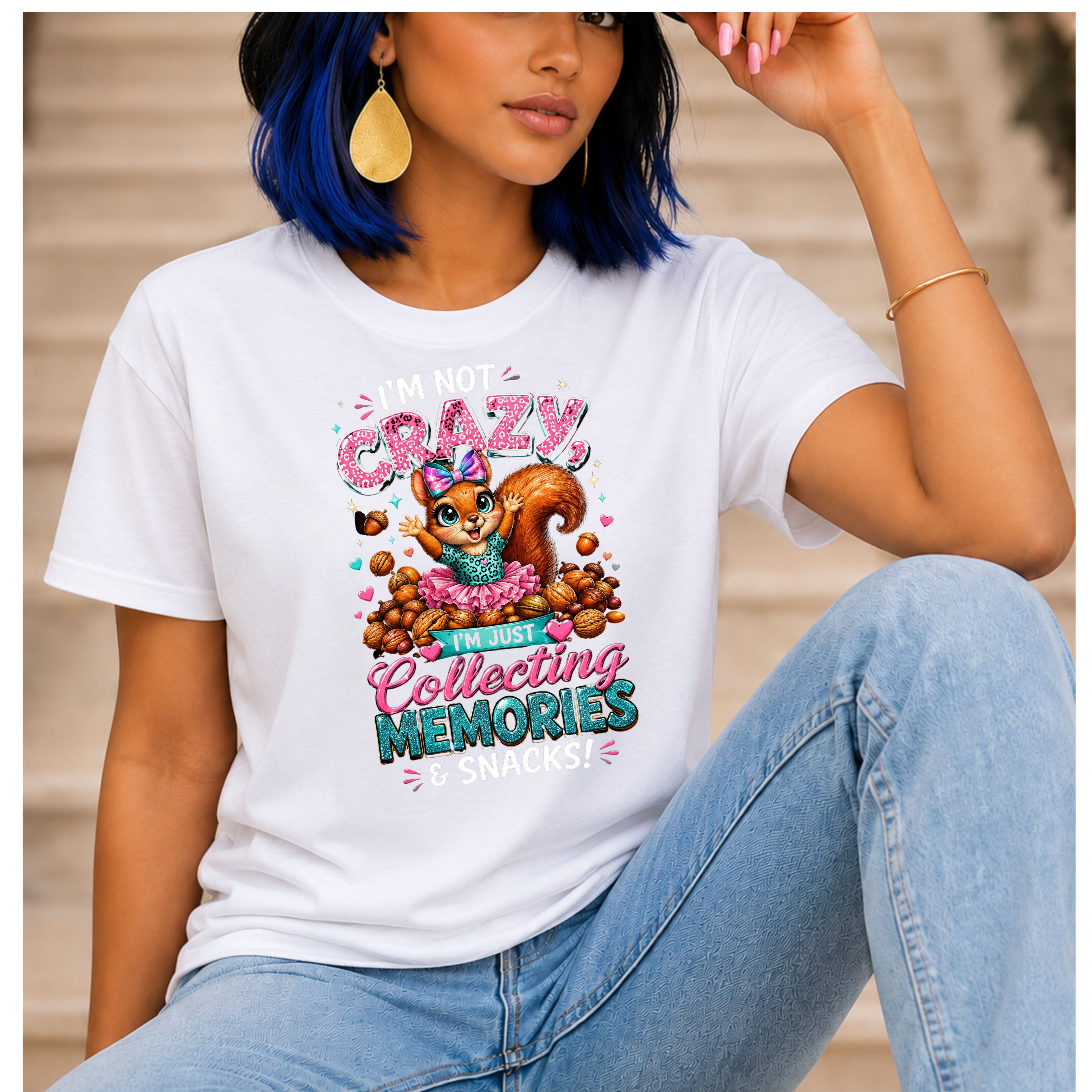 A woman wearing a white graphic t-shirt with a colorful cartoon squirrel design and the text 'I'm Not Crazy, I'm Just Collecting Memories & Snacks'.