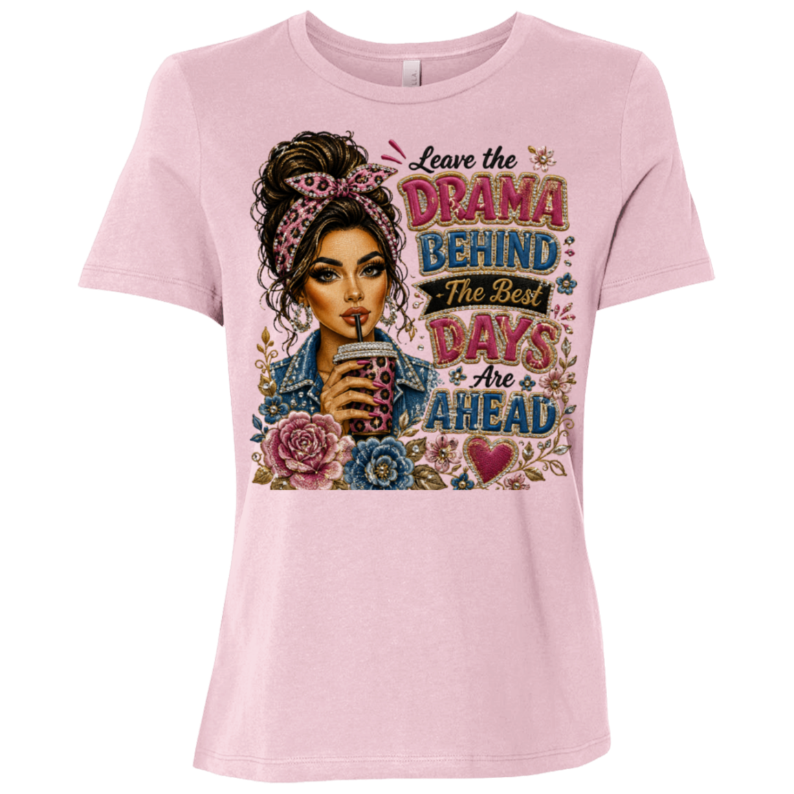 A light pink short-sleeve t-shirt with a colorful graphic print on the front. The graphic features an illustration of a woman with her hair in a messy bun, holding a drink, surrounded by flowers and the text 'Leave the DRAMA BEHIND The Best DAYS & Are AHEAD'.