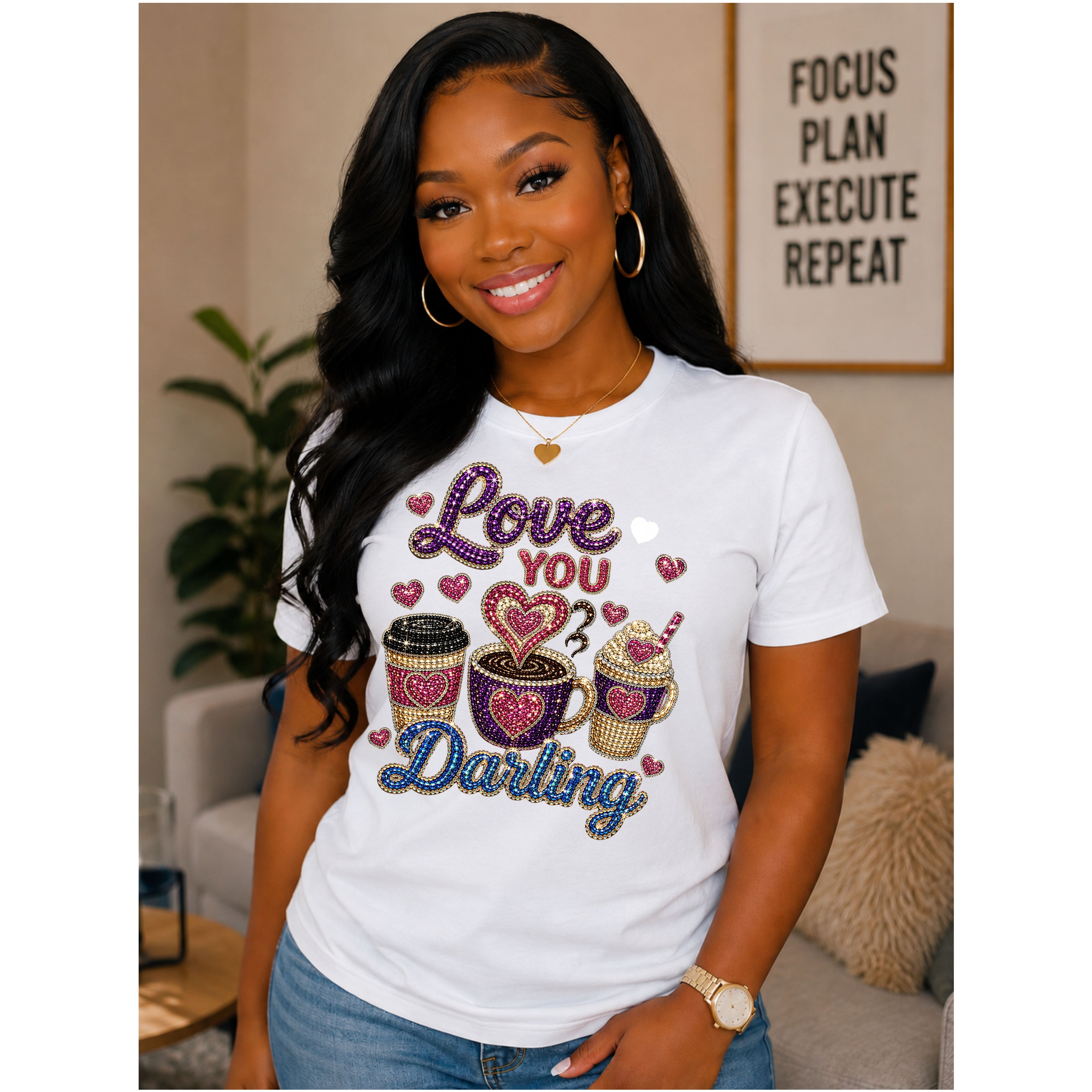 A woman wearing a white graphic t-shirt with 'Love You Darling' written in rhinestone-style lettering alongside coffee cup and cupcake illustrations, posed in a living room setting.