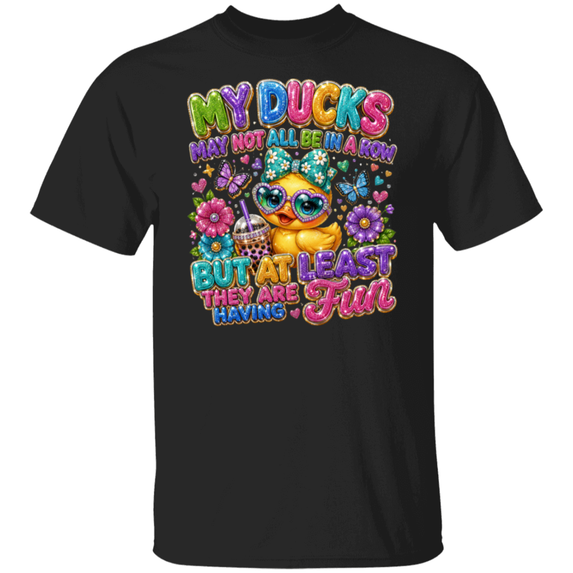 A black short-sleeve crewneck t-shirt featuring a colorful graphic print of a cute cartoon duck wearing sunglasses and a hat, surrounded by flowers, butterflies, and the text 'MY DUCKS MAY NOT ALL BE A KIN BUT AT LEAST FUN THEY ARE HAVING'.