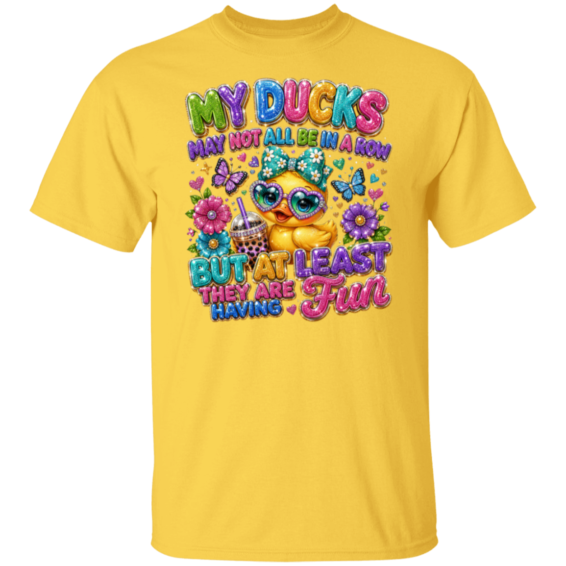 A daisy color short-sleeve crewneck t-shirt featuring a colorful graphic print on the front. The graphic shows a cute cartoon duck wearing sunglasses and a glittery bow, surrounded by flowers, butterflies, and the text 'MY DUCKS MAY NOT ALL BE IN A ROW BUT AT LEAST THEY ARE HAVING Fun'.