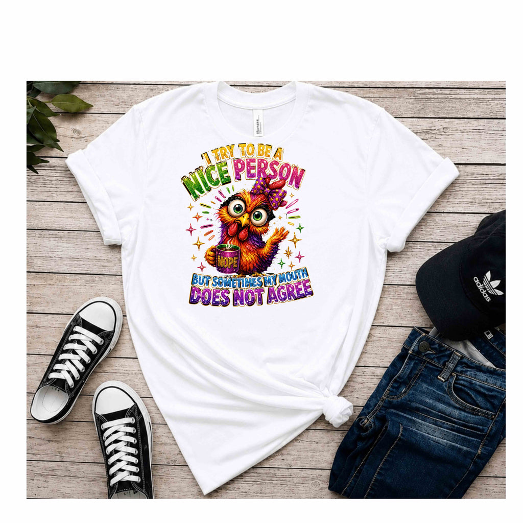 A white graphic t-shirt laid flat on a light wood background, styled with black sneakers, blue jeans, and a black Adidas cap. The t-shirt features a colorful cartoon owl and the text 'I TRY TO BE A NICE PERSON BUT SOMETIMES MY MOUTH DOES NOT AGREE'.