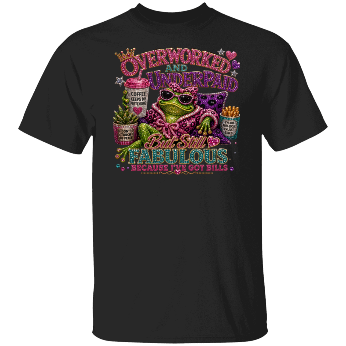 A black short-sleeve t-shirt with a colorful graphic print on the front. The graphic features a green frog wearing sunglasses and a pink leopard-print shirt, surrounded by text that reads 'OVERWORKED AND UNDERPAID But Still FABULOUS BECAUSE I'VE GOT BILLS' along with coffee cups, a plant, and fries.