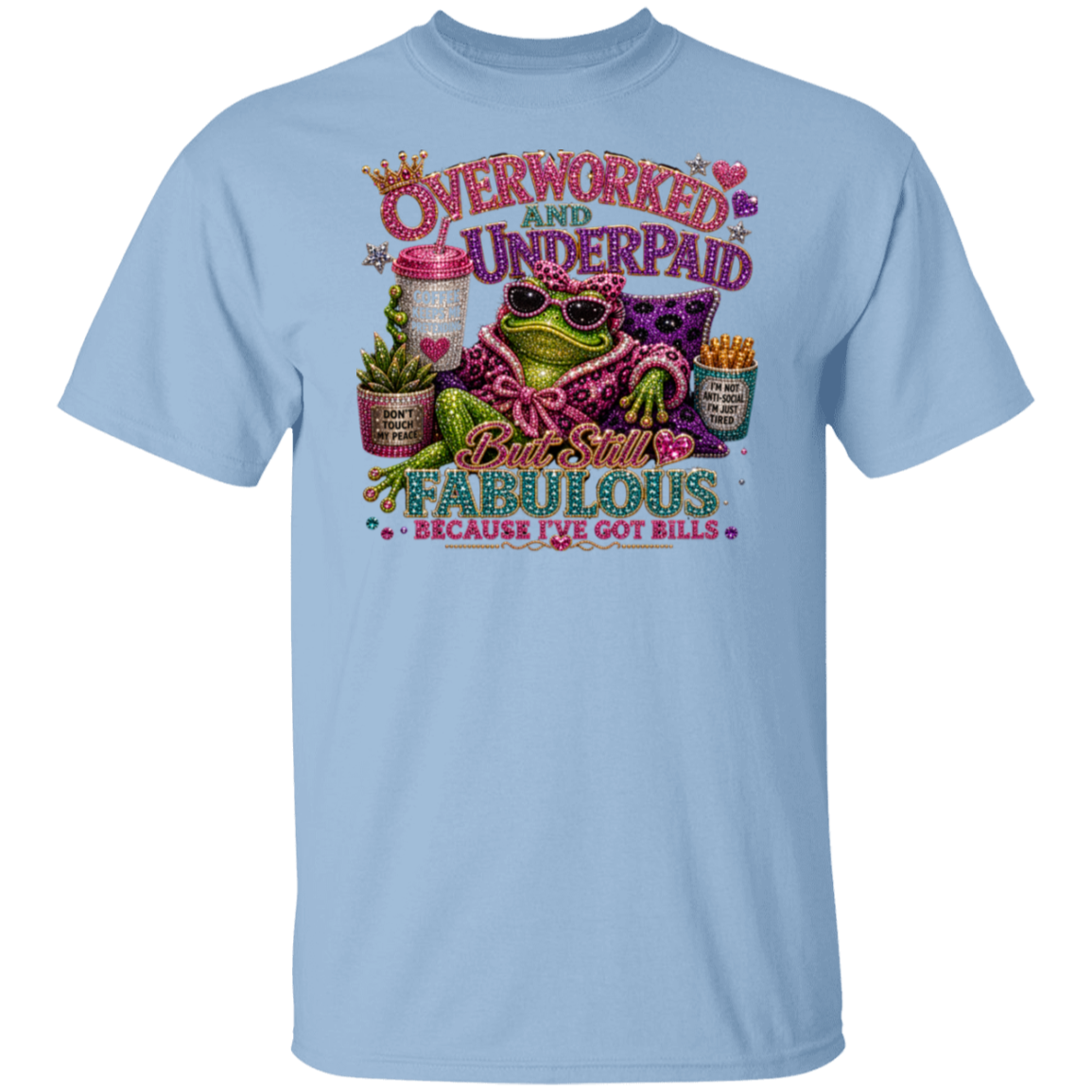 A light blue crewneck t-shirt featuring a colorful graphic print of a frog wearing sunglasses and a pink patterned shirt, surrounded by text that reads 'Overworked and Underpaid But Still Fabulous Because I've Got Bills'.