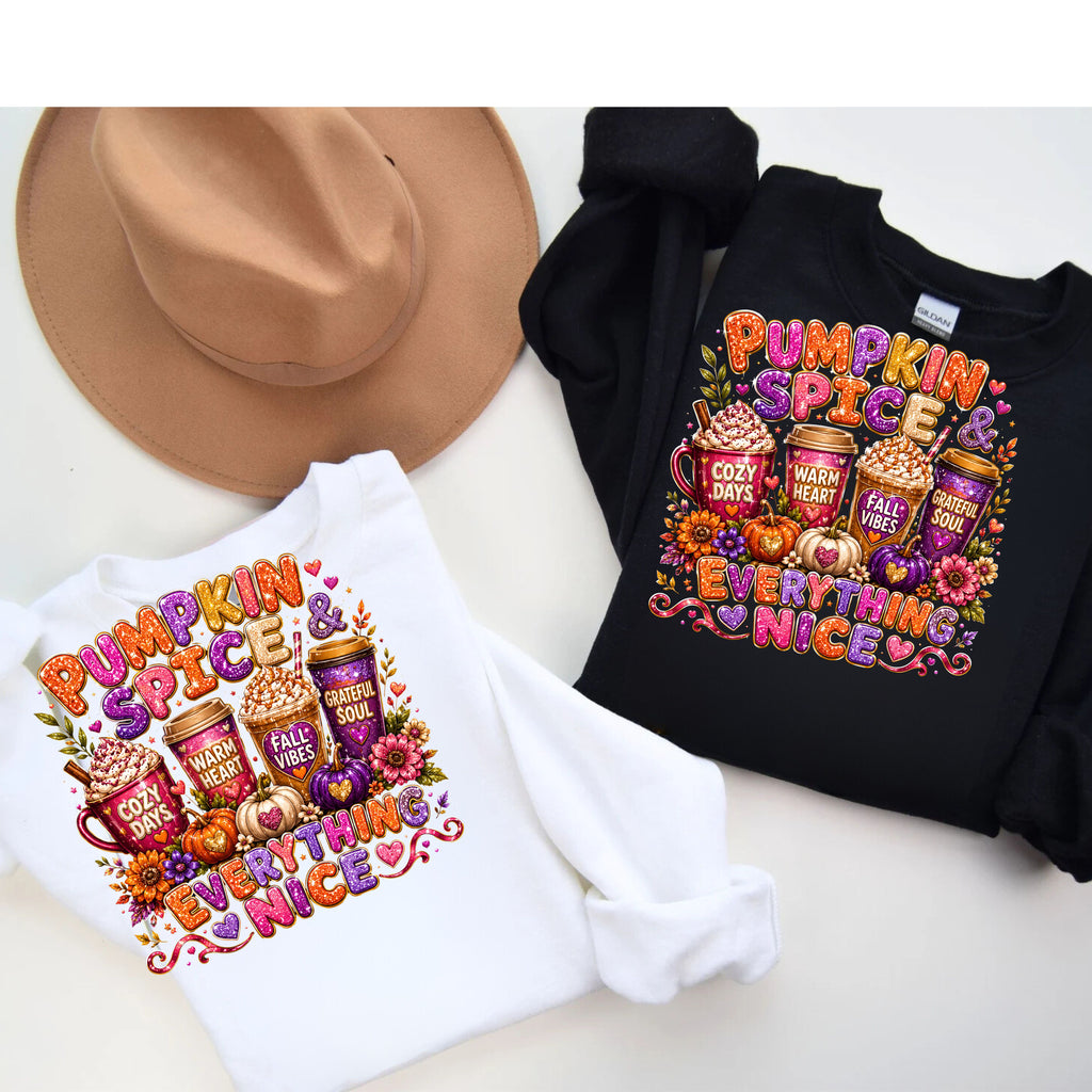 Two long-sleeve graphic sweatshirts, one white and one black, displayed flat with a tan wide-brim hat on a light beige background. The sweatshirts feature a colorful 'Pumpkin Spice & Everything Nice' graphic with coffee cups, pumpkins, and fall leaves.