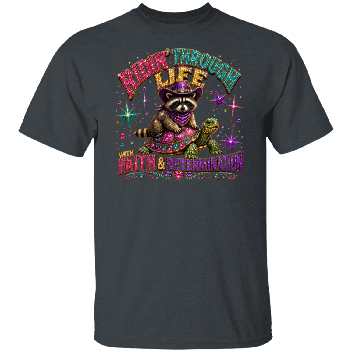 A dark heather gray t-shirt featuring a colorful graphic of a raccoon riding a turtle with the text 'RIDE THROUGH LIFE WITH FAITH & DETERMINATION' in a stylized, glittery font.