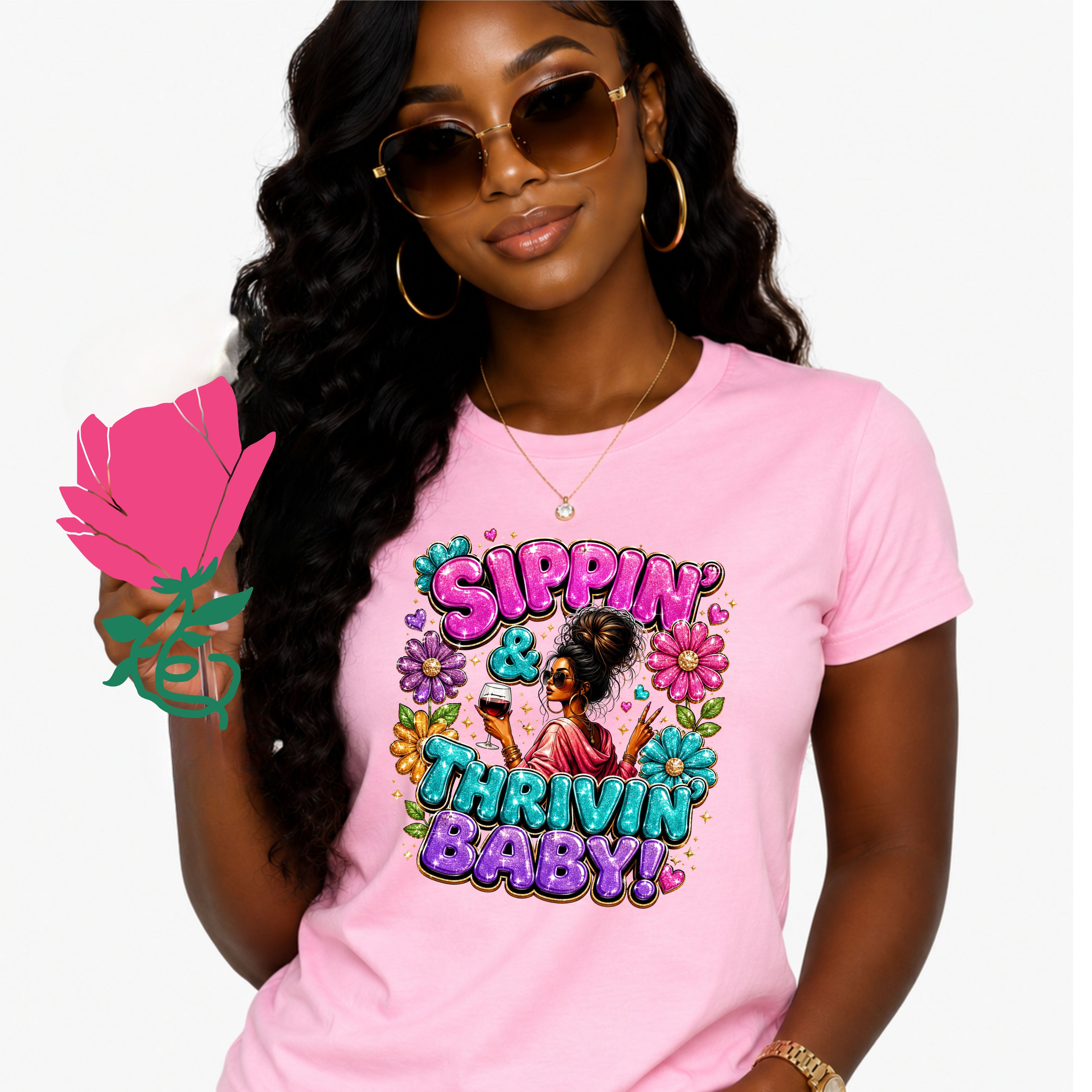 A woman wearing a light pink graphic t-shirt with a colorful 'Sippin' & Thrivin' Baby!' design, styled with gold hoop earrings and sunglasses, holding a pink rose against a white background.
