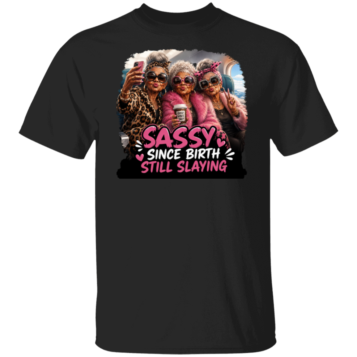 A black short-sleeve crewneck t-shirt featuring a colorful graphic print of three elderly women taking a selfie, with the text 'SASSY SINCE BIRTH STILL SLAYING' in pink and white lettering.
