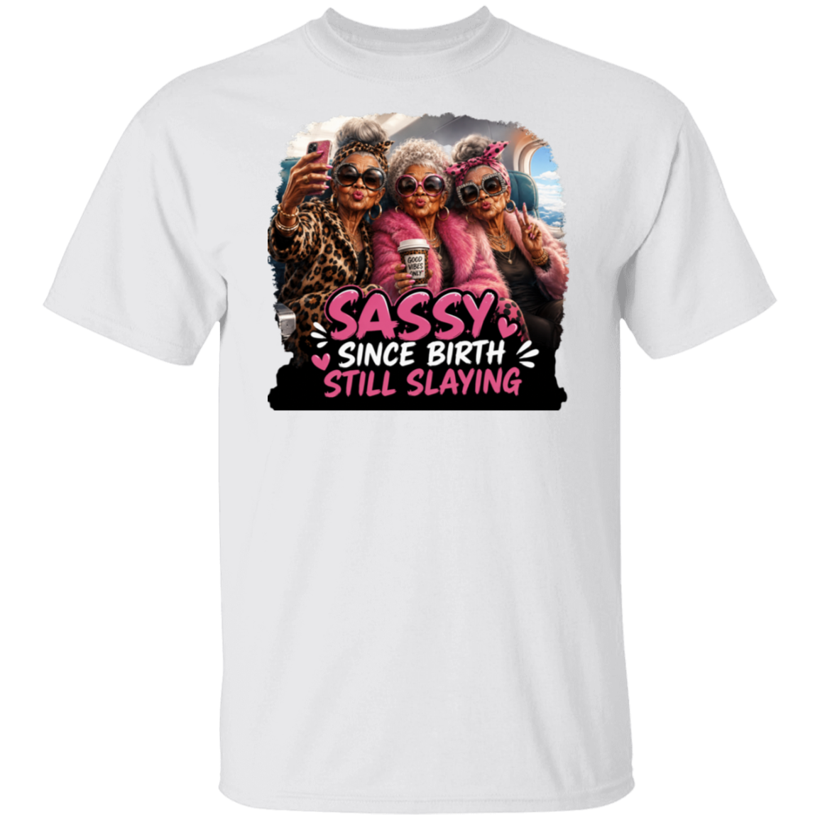 A white short-sleeve crewneck t-shirt featuring a colorful graphic print of three elderly women taking a selfie with the text 'SASSY SINCE BIRTH STILL SLAYING' in pink and white lettering.