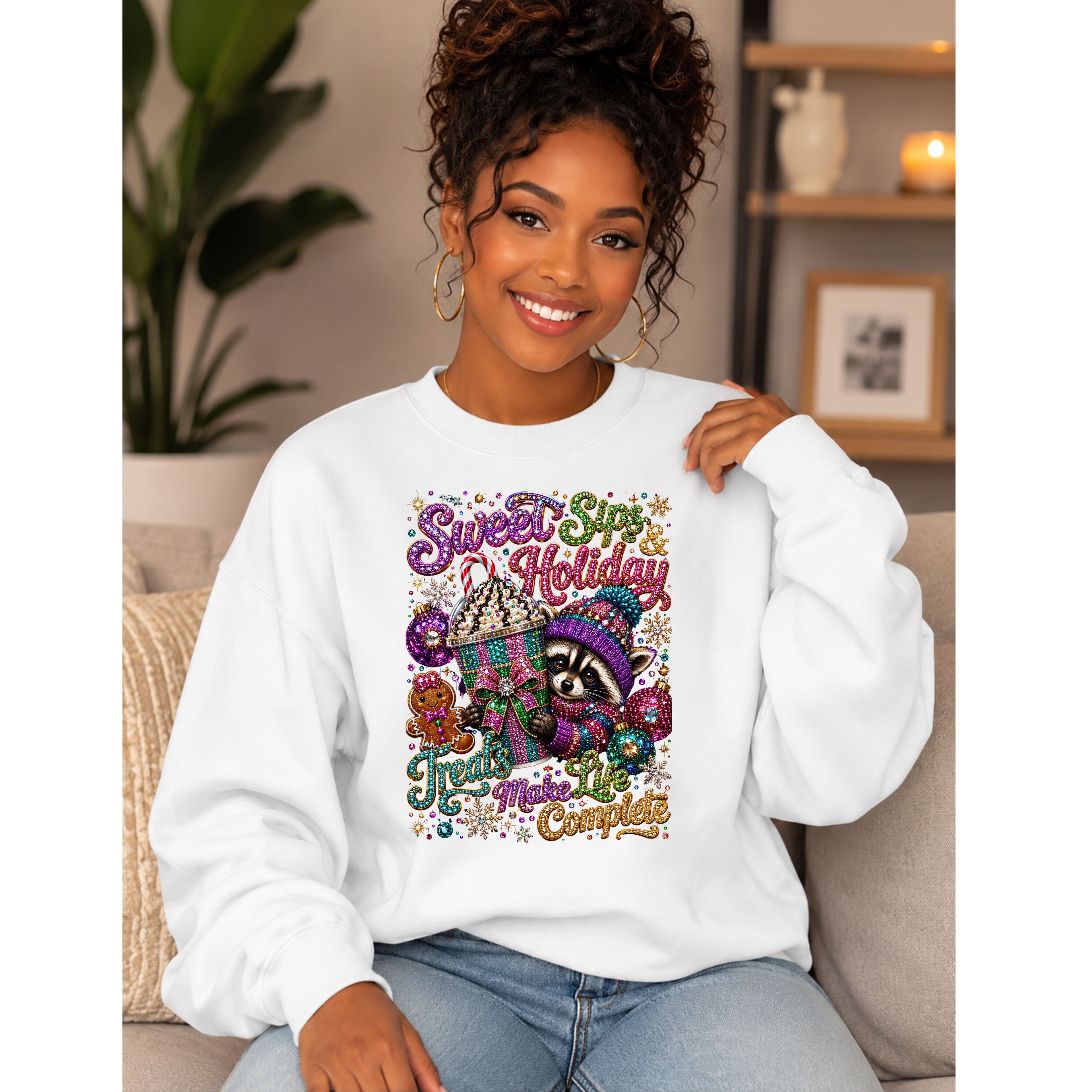 A woman wearing a white crewneck sweatshirt with a colorful 'Sweet Spot Holiday' raccoon graphic, sitting on a beige couch in a cozy living room setting.