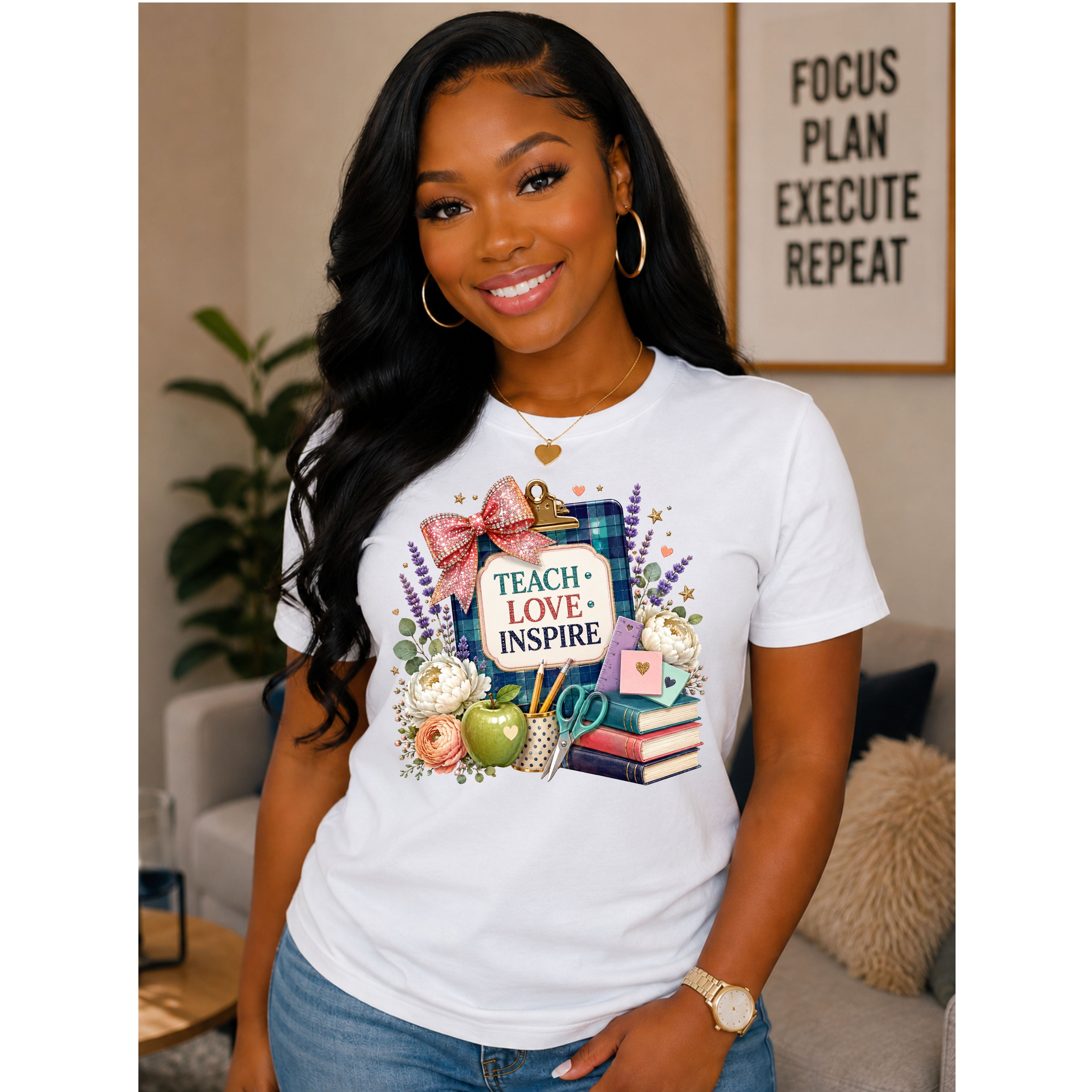 A woman wearing a white graphic t-shirt with a colorful design featuring books, an apple, a pink bow, and the words 'TEACH LOVE INSPIRE'. She is posing in a cozy living room setting.