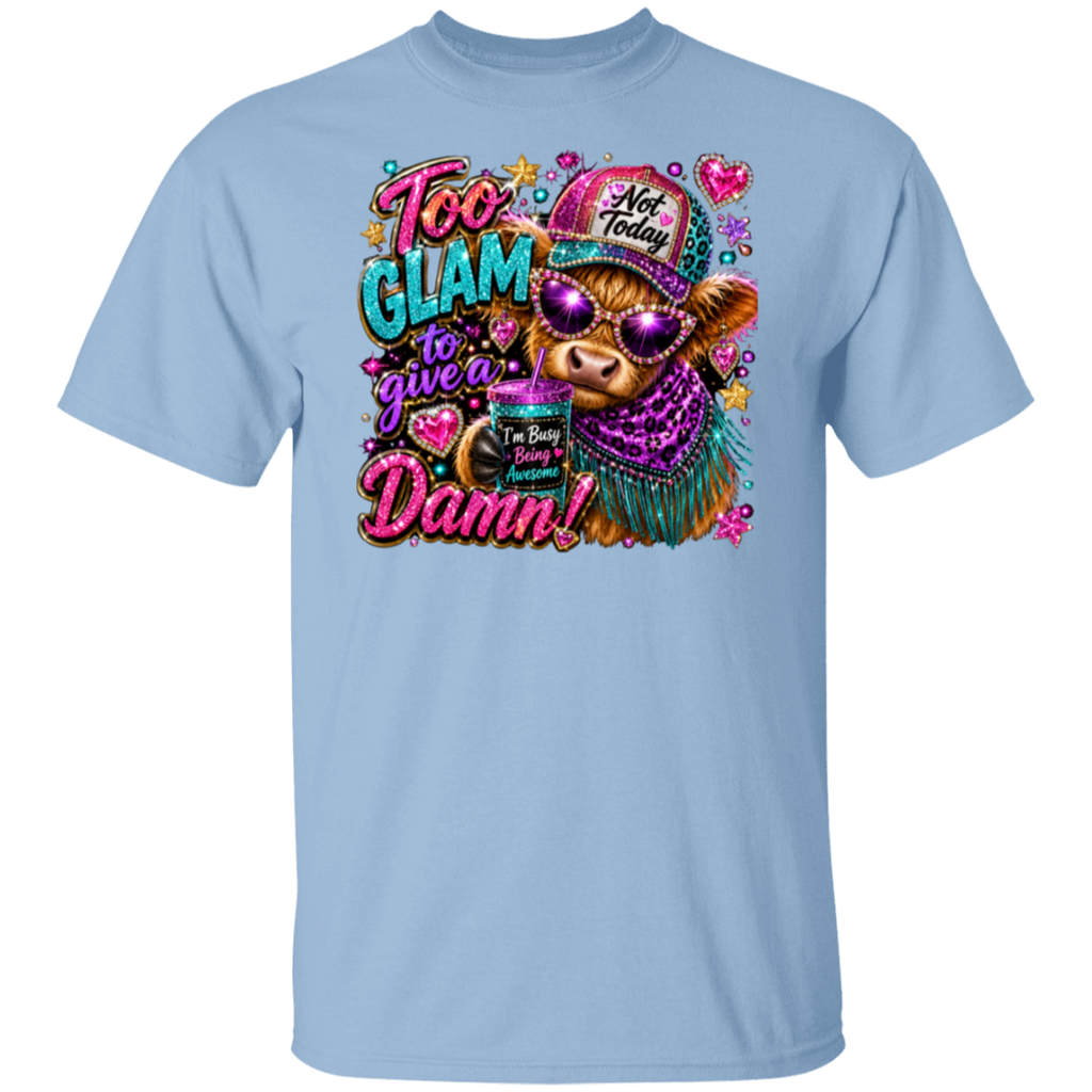 A light blue crewneck t-shirt featuring a colorful graphic print of a cow wearing sunglasses and a hat with the text 'Too Glam to give a Damn!'.