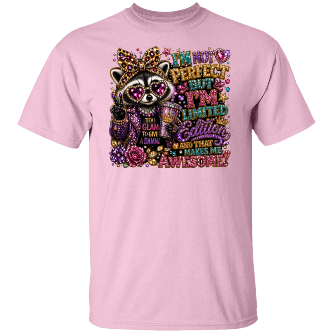 A light pink short-sleeve crewneck t-shirt featuring a colorful graphic of a crowned raccoon wearing sparkly sunglasses and holding a drink, surrounded by decorative text that reads 'I'm not perfect but I'm limited edition glittery and that makes me awesome!'.