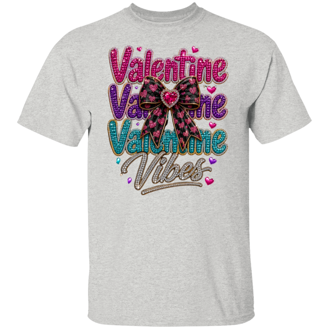 An ash color short-sleeve t-shirt featuring a colorful graphic on the front with the text 'Valentine Valentine Valentine Vibes' in pink, purple, and teal glitter-style lettering, accented by a pink and black plaid bow with a red heart in the center.