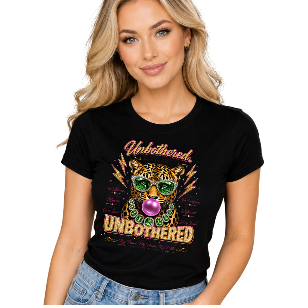 A woman wearing a black graphic t-shirt with a leopard wearing green sunglasses and blowing a pink bubblegum bubble, with the text 'Unbothered. UNBOOTHERED' in gold and green.